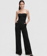 Full-body studio view of a model wearing a black strapless wide-leg jumpsuit